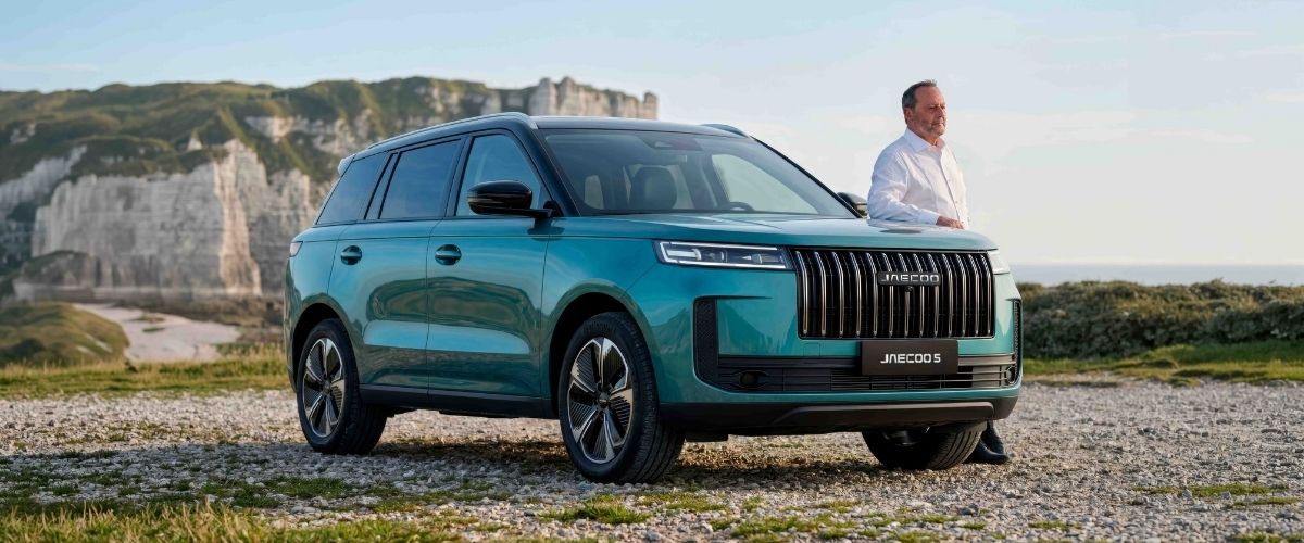 Doğada, deniz kenarındaki kayalık bir alanda park halinde duran yeşil renkli JAECOO 5 SUV modeli ve yanında manzarayı izleyen bir adam.