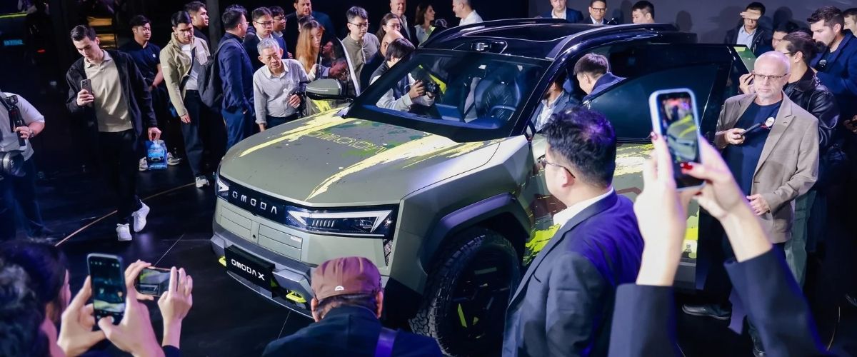 OMODA X Night etkinliğinde sahnede sergilenen, yeşil ve sarı detaylı yeni nesil fütüristik OMODA X SUV modelini inceleyen ve fotoğraflayan basın mensupları.